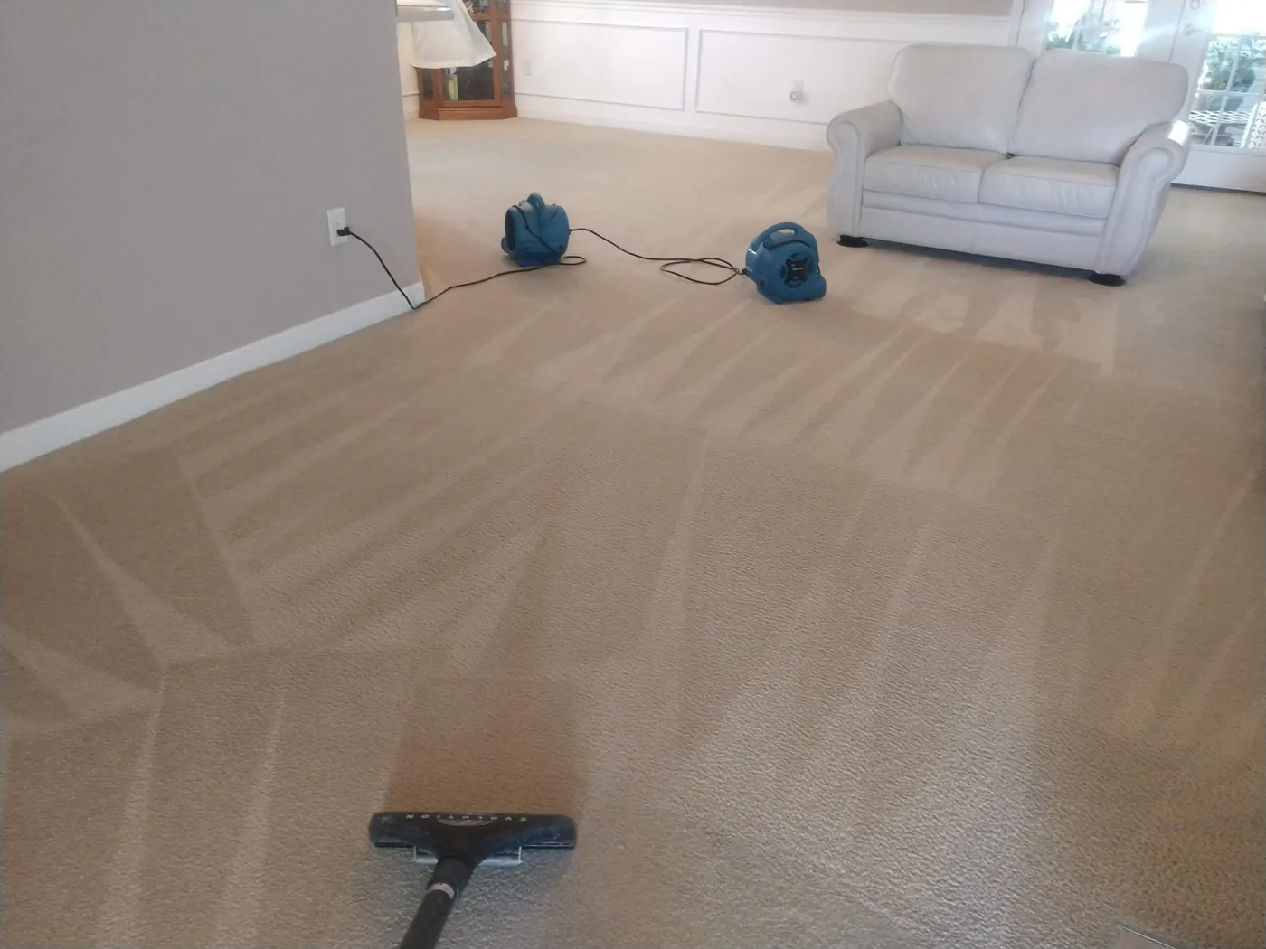 Two air movers drying a cleaned living room carpet in front of a white sofa.