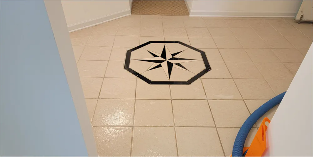 Before: an entry tile floor with a compass rose inlay and dingy grout, the cleaning hose beside it.