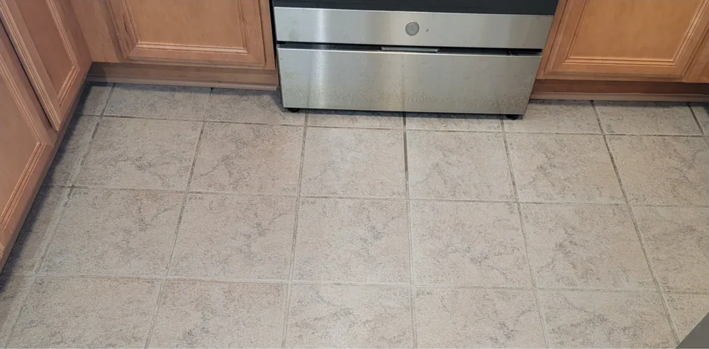 Before: a kitchen tile floor with gray, uneven grout by the oven.