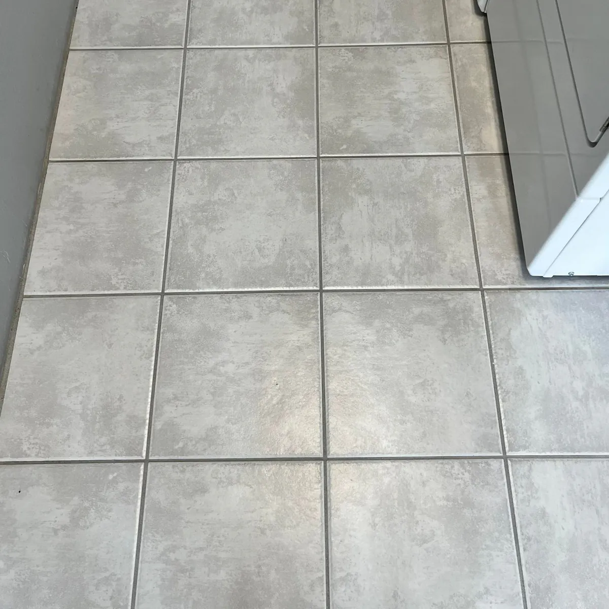Before: gray square floor tiles in a laundry room with dark, dirty grout lines.