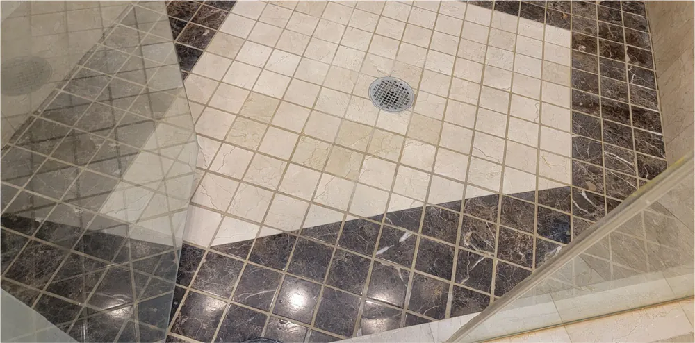 Before: a marble shower floor with a dark border, the grout dull.