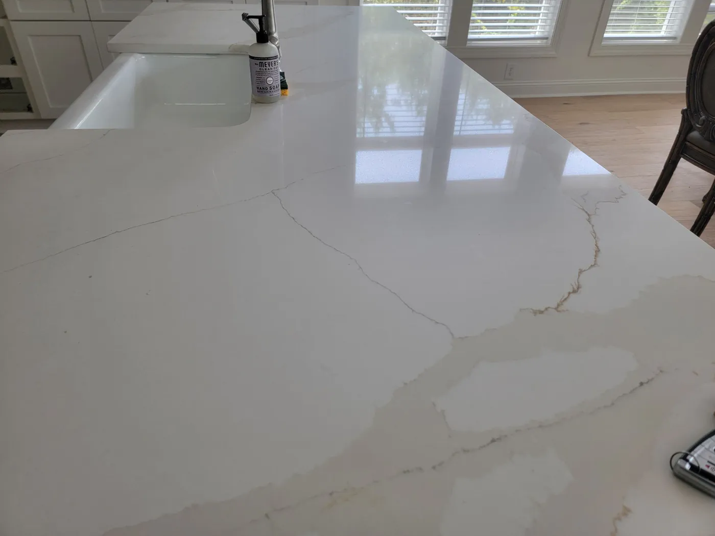 A white kitchen countertop with soft veining beside a farmhouse sink.