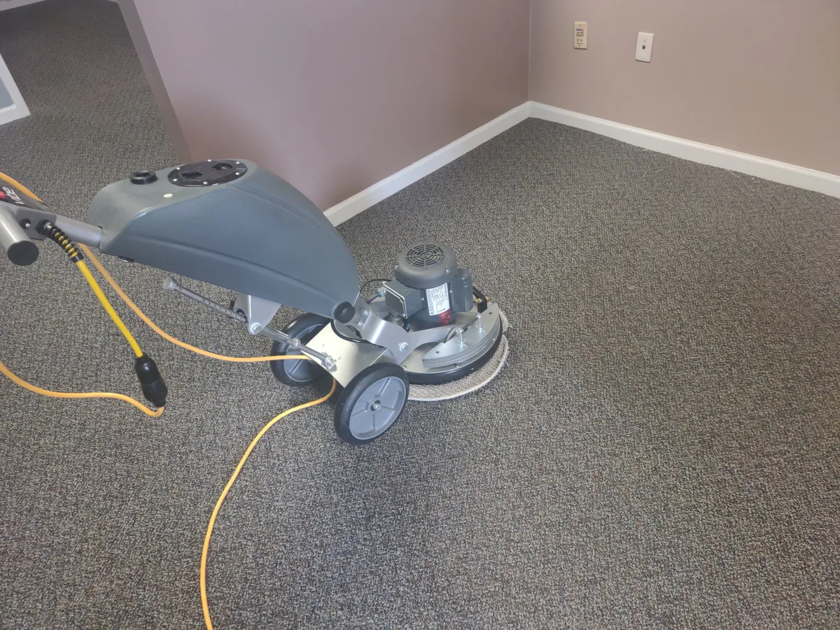 A rotary cleaning machine on a gray carpet.