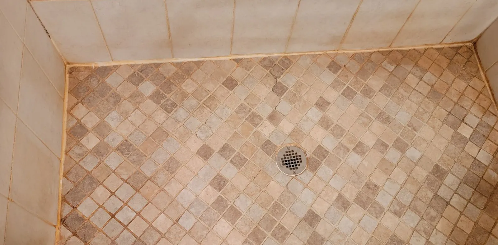 Before: a diamond mosaic shower floor with rust-orange stains in the grout and along the edges.