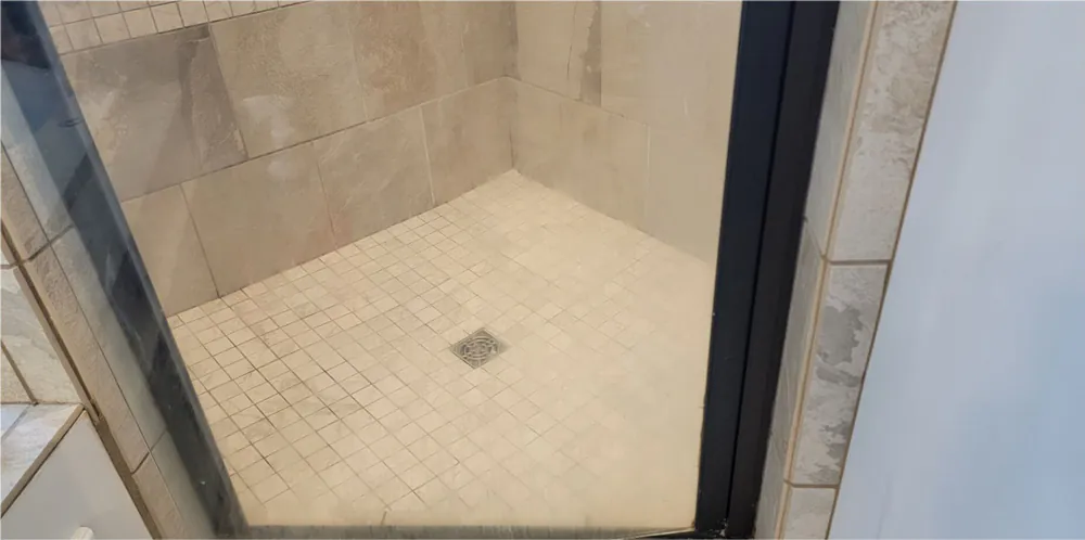 Before: a corner shower behind glass, tile and grout dull.