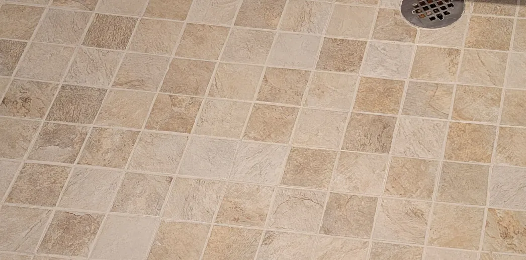 Before: a tan tile shower floor with dark grout around the drain.